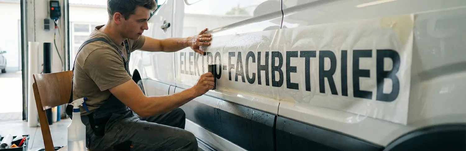 Ein Mann rakelt seine Werbebeschriftung nass auf einen Lieferwagen